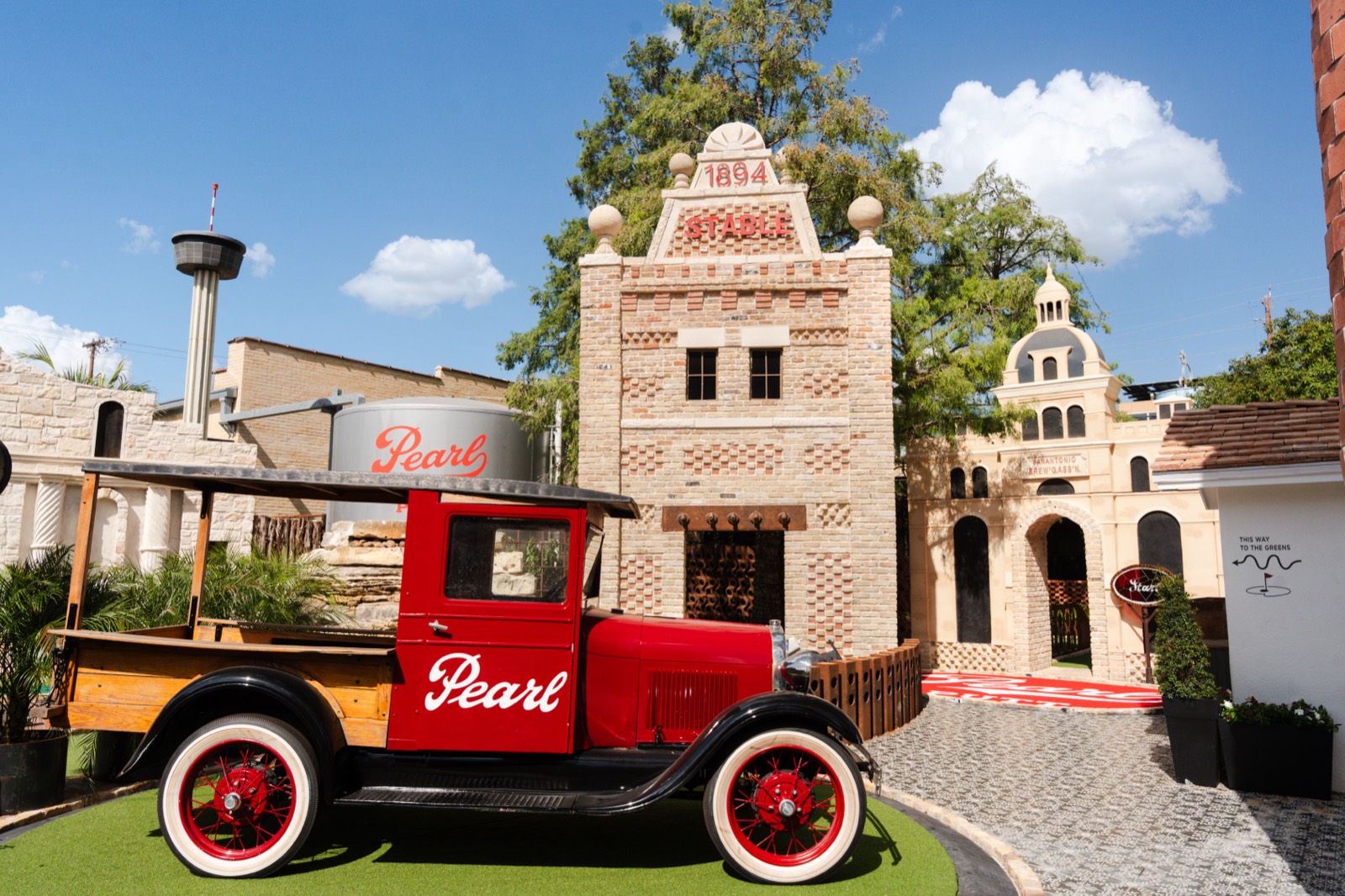 Vintage red Pearl delivery truck in front of the brick brewery replica, with the Tower of the Americas beyond